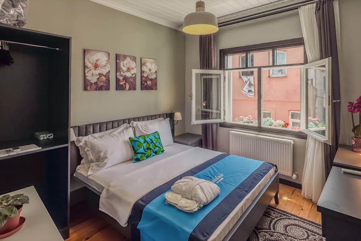 Quarto de hotel com cama, escrivaninha, janela com cortinas e vista para o exterior.