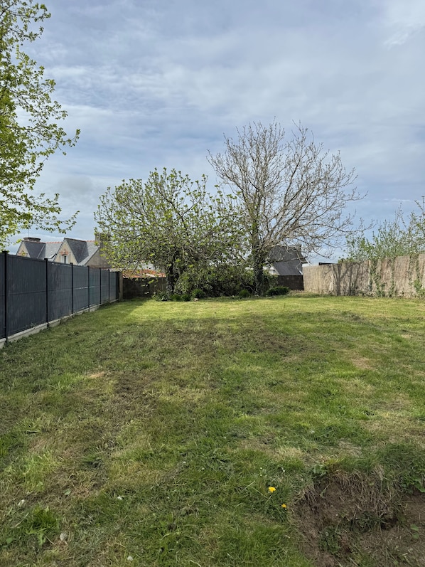 A grassy backyard with a fence, trees, and a building in the background. - Just minutes from everything! Family townhouse close to all amenities (Bannalec)