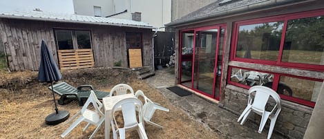 A backyard with a wooden deck, a dining area with plastic chairs, and a red-framed glass door.