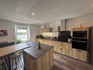 A modern kitchen with wooden cabinets, a central island, bar stools, a microwave, and a built-in oven. - Just a few minutes from everything! Family Townhouse Close to All Amenities (Bannalec)