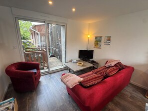 A living room with a red sofa, a red armchair, a television, and a sliding glass door leading to an outdoor area. - Just a few minutes from everything! Family Townhouse Close to All Amenities (Bannalec)