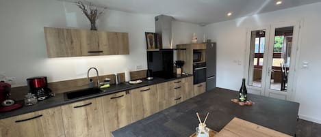 A modern kitchen with wooden cabinets, a black countertop, and a dining area with a wooden table.