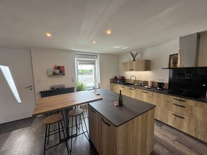 A modern kitchen with a central island, wooden cabinets, and a black countertop. - Just a few minutes from everything! Family Townhouse Close to All Amenities (Bannalec)