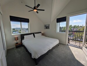 Ein Schlafzimmer mit einem Bett, zwei Nachttischlampen, einem Deckenventilator und Blick auf die Stadt durch große Fenster.