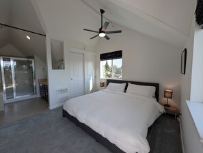 Ein Schlafzimmer mit Bett, Deckenventilator, Fenster mit Aussicht und einer Schiebeglastür, die auf einen Balkon führt.