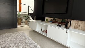 Moderni olohuone, jossa on seinälle asennettu litteänäyttöinen televisio tummalla seinällä, valkoinen hyllykkö, harmaa matto ja ruskea tuoli.