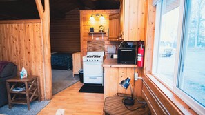 A compact wooden cabin with a kitchenette, a bed, and a window. - Beautiful 1-bedroom cabin in Kenai. Perfect for a getaway or fishing trip! (Kenai)