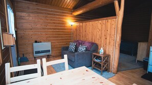 A cozy cabin interior with a wooden wall, a couch, a small table, and a heater. - Beautiful 1-bedroom cabin in Kenai. Perfect for a getaway or fishing trip! (Kenai)
