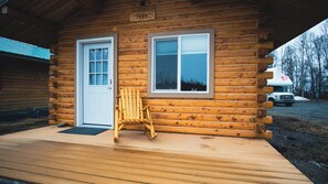 Une cabane en rondins avec une véranda en bois, une porte blanche et une fenêtre.