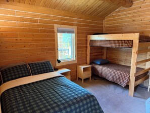 Une chambre de style cabane avec un lit superposé, un lit simple, une petite table et une fenêtre.