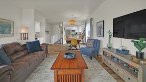 A living room with a brown leather sofa, a blue armchair, a wooden coffee table, and a TV on the wall. - Marina-Front Retreat - Steps to Beach, Wine & Water (Algoma)