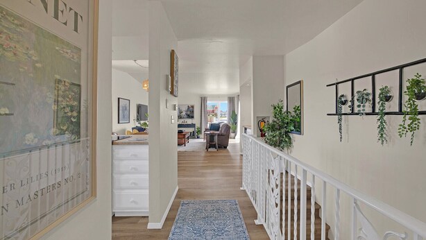 A hallway with a white railing, a blue patterned rug, and a dining area in the background. - Marina-Front Retreat - Steps to Beach, Wine & Water (Algoma)