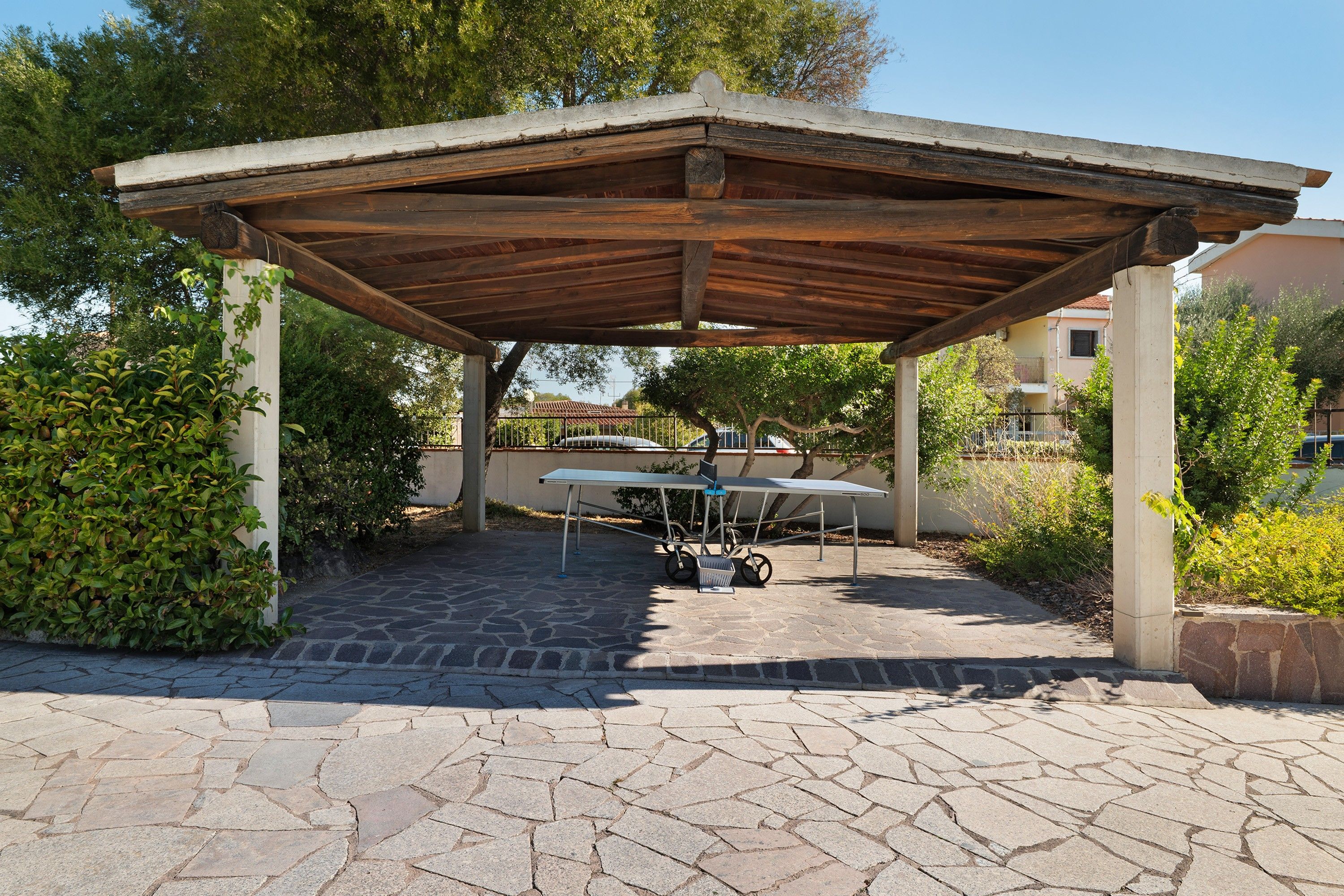 A covered outdoor seating area with a stone floor, a table with chairs, and a bicycle parked underneath.
