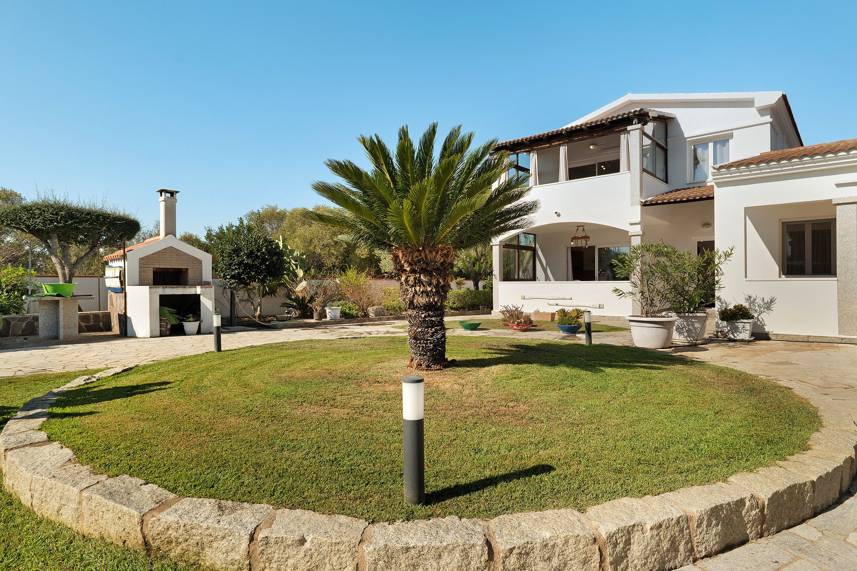 A two-story building with a white facade, a stone pathway, and a palm tree in the center.