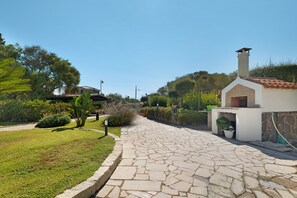 A paved pathway leading to a building with a chimney, surrounded by greenery and a clear sky. - Apartment 'Annina' with Private Terrace, Wi-Fi and Air Conditioning (Pittulongu)