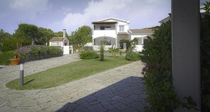 Un patio con un sendero empedrado, un edificio blanco y abundante vegetación.