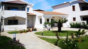 A white building with a tiled roof, a paved pathway, and a well-maintained garden. - Apartment 'Annina' with Private Terrace, Wi-Fi and Air Conditioning (Pittulongu)