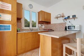 A compact kitchen with wooden cabinets, a microwave, and a window. - Apartment 'Annina' with Private Terrace, Wi-Fi and Air Conditioning (Pittulongu)
