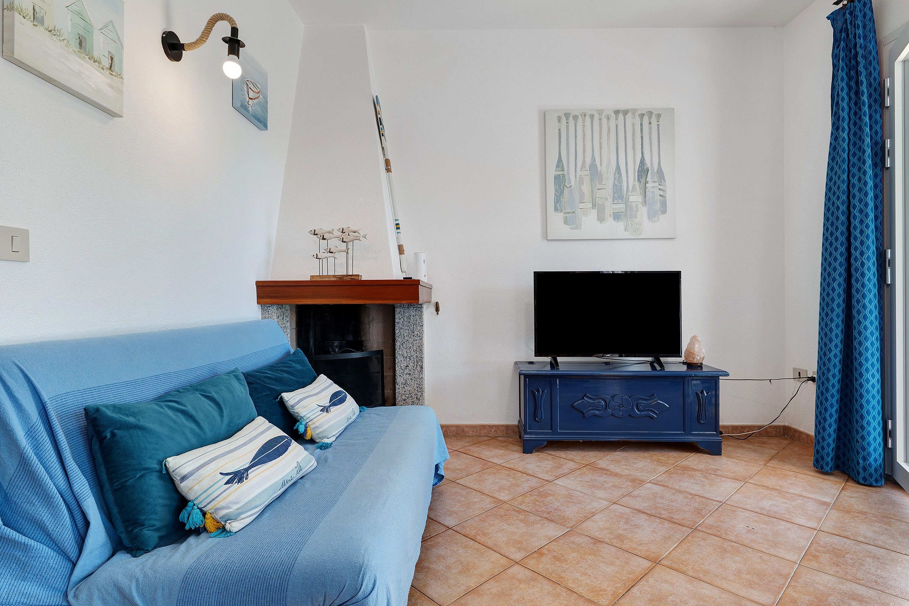 Ein Wohnzimmer mit einem blauen Sofa, einem Kamin, einem Flachbildfernseher und Kunstwerken an den Wänden.