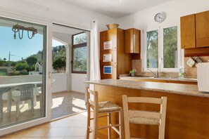 A kitchen with wooden cabinets, a built-in island, and a dining area with chairs. - Apartment 'Annina' with Private Terrace, Wi-Fi and Air Conditioning (Pittulongu)