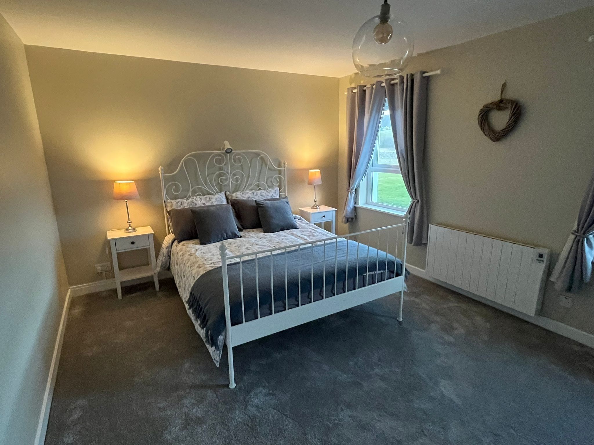A bedroom with a metal bed frame, two bedside tables with lamps, a window with curtains, and a radiator.