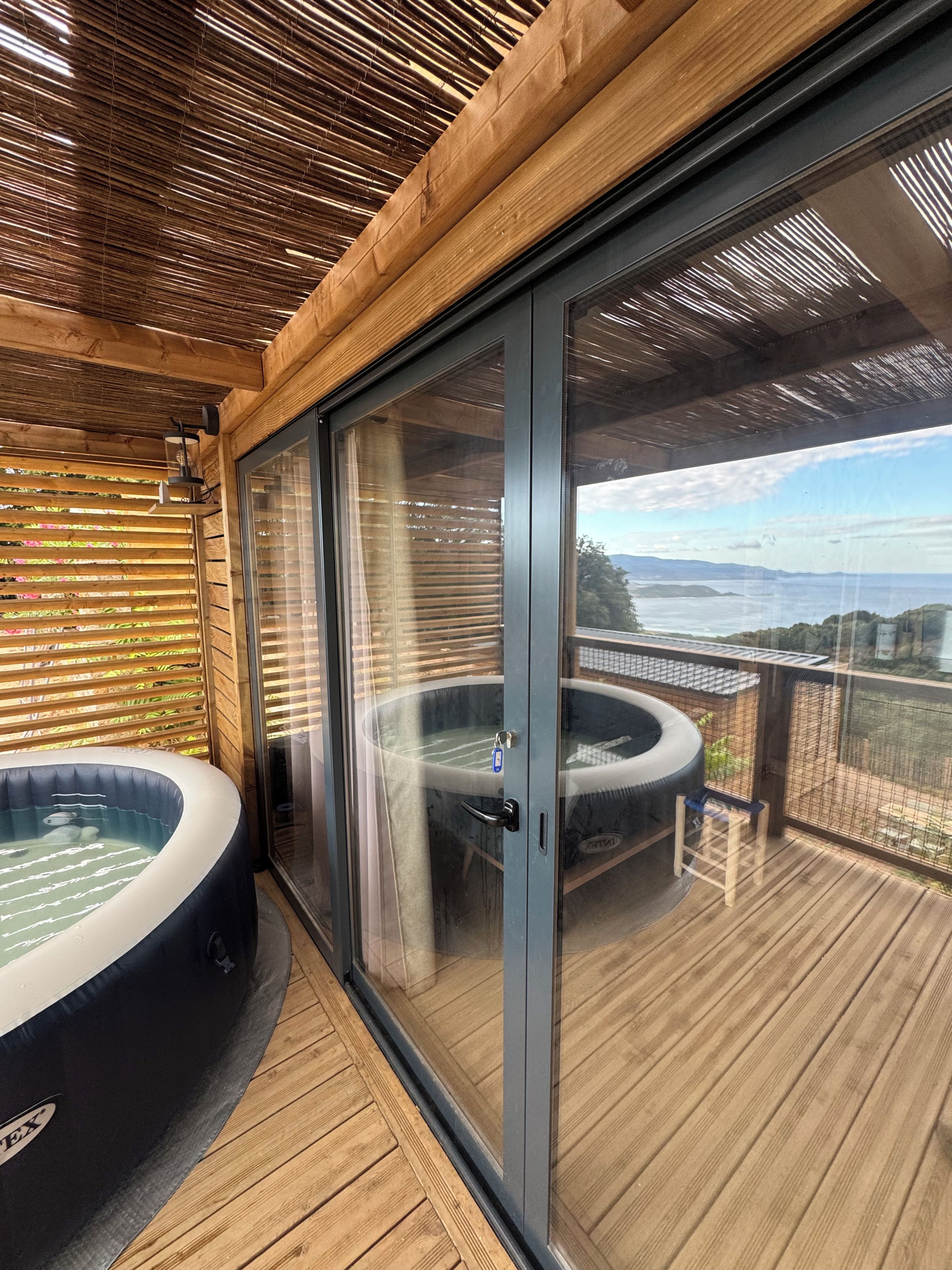 Una terraza de madera con un jacuzzi y una puerta de cristal que da a una vista panorámica.