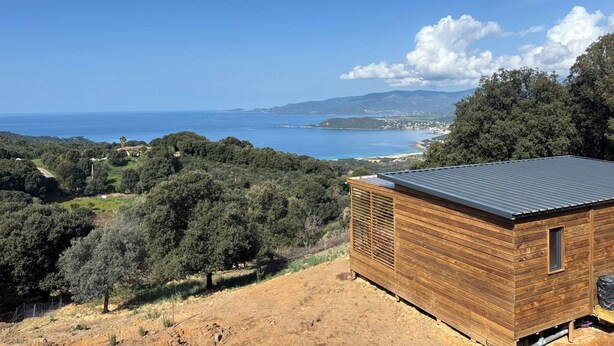 Une cabane en bois avec un toit en métal, entourée d’arbres et offrant une vue sur la mer.