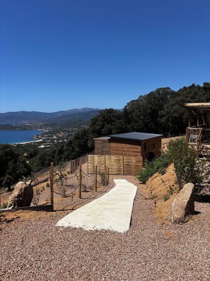 A modern building with a wooden exterior, a gravel pathway leading to it, and a view of a coastal landscape in the background.