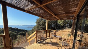 Une terrasse en bois avec une enceinte en verre, des meubles d’extérieur et une vue sur la mer et les collines.