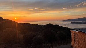 Une vue sur le coucher de soleil, avec un paysage côtier, des collines et un bâtiment en bois.
