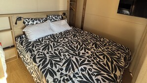 Un lit avec une couvre-lit à motifs floraux, une tête de lit en bois, un téléviseur fixé au mur et un luminaire suspendu au plafond.