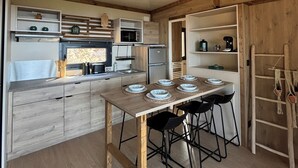 Une cuisine moderne avec des poutres en bois, un îlot central doté de tabourets, des appareils électroménagers intégrés et un luminaire suspendu.