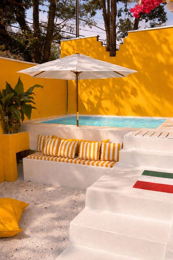 A pool area with a white umbrella, a sofa with striped cushions, and a small pool.