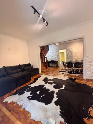 A living room with a black sofa, a cowhide rug, a staircase, and a dining area with chairs.