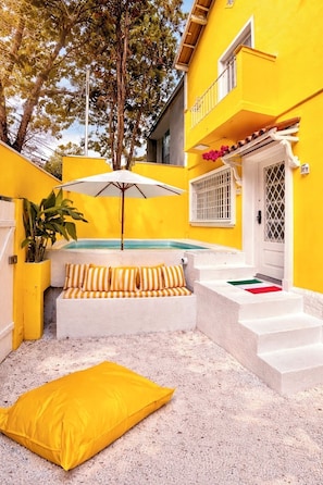 A yellow building with a pool, a white door, and a staircase leading to a balcony.