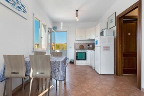 A compact kitchen with a dining area, a view through the window, and a door with a sign. - Apartment 'Zio Tonino' with Private Terrace, Wi-Fi and Air Conditioning (Pittulongu)