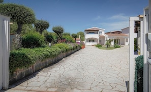 Una calle residencial con pavimento de piedra, casas blancas y abundante vegetación.