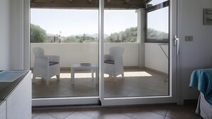 A balcony with two white wicker chairs, a small table, and a view of trees and hills. - Apartment 'Zio Tonino' with Private Terrace, Wi-Fi and Air Conditioning (Pittulongu)