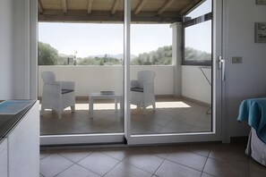 A balcony with two white wicker chairs, a small table, and a view of trees and hills. - Apartment 'Zio Tonino' with Private Terrace, Wi-Fi and Air Conditioning (Pittulongu)