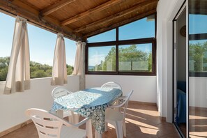 Eine überdachte Terrasse mit Tisch und Stühlen und Blick auf Grünflächen, sowie eine Schiebetür.
