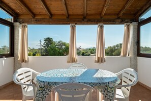 A covered outdoor seating area with a round table and chairs, a view of greenery and buildings in the distance. - Apartment 'Zio Tonino' with Private Terrace, Wi-Fi and Air Conditioning (Pittulongu)
