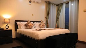 A hotel room with a bed, a nightstand, a lamp, a window with curtains, and a view of the outside.