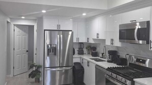 A modern kitchen with stainless steel appliances, white cabinetry, and a large island. - Stylish Secondary Suite with Private Entry (Airdrie)