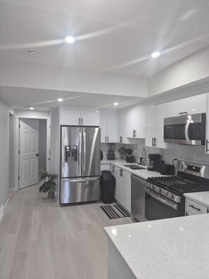 A modern kitchen with stainless steel appliances, white cabinetry, and a large island. - Stylish Secondary Suite with Private Entry (Airdrie)