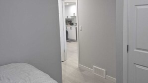 A bedroom with a bed, a door, and a hallway leading to a kitchen area. - Stylish Secondary Suite with Private Entry (Airdrie)