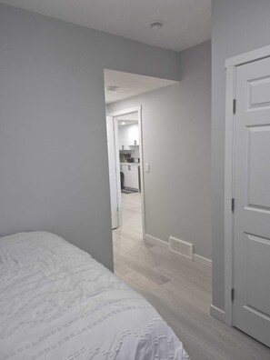 A bedroom with a bed, a door, and a hallway leading to a kitchen area. - Stylish Secondary Suite with Private Entry (Airdrie)