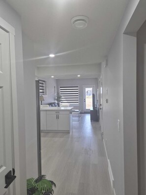 A hallway leading to a kitchen with a window, a door, and a ceiling light. - Stylish Secondary Suite with Private Entry (Airdrie)