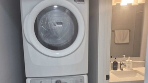 A stacked washer and dryer in a bathroom with a sink and towel rack. - Stylish Secondary Suite with Private Entry (Airdrie)