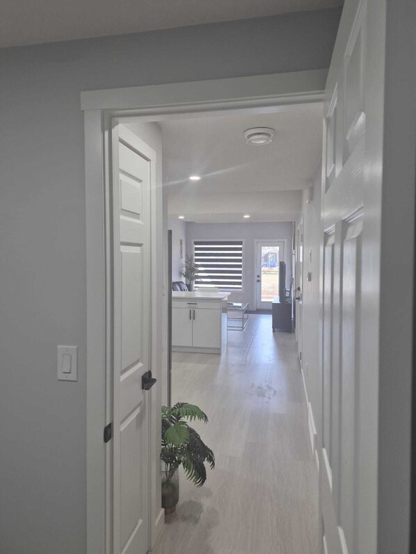 A hallway with a door on the left, a potted plant, and a window with blinds in the background. - Stylish Secondary Suite with Private Entry (Airdrie)