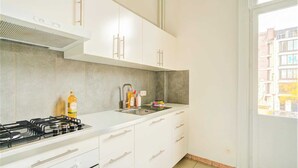 Una cuina moderna amb armaris blancs, fogó de gas i finestra amb vista a edificis.